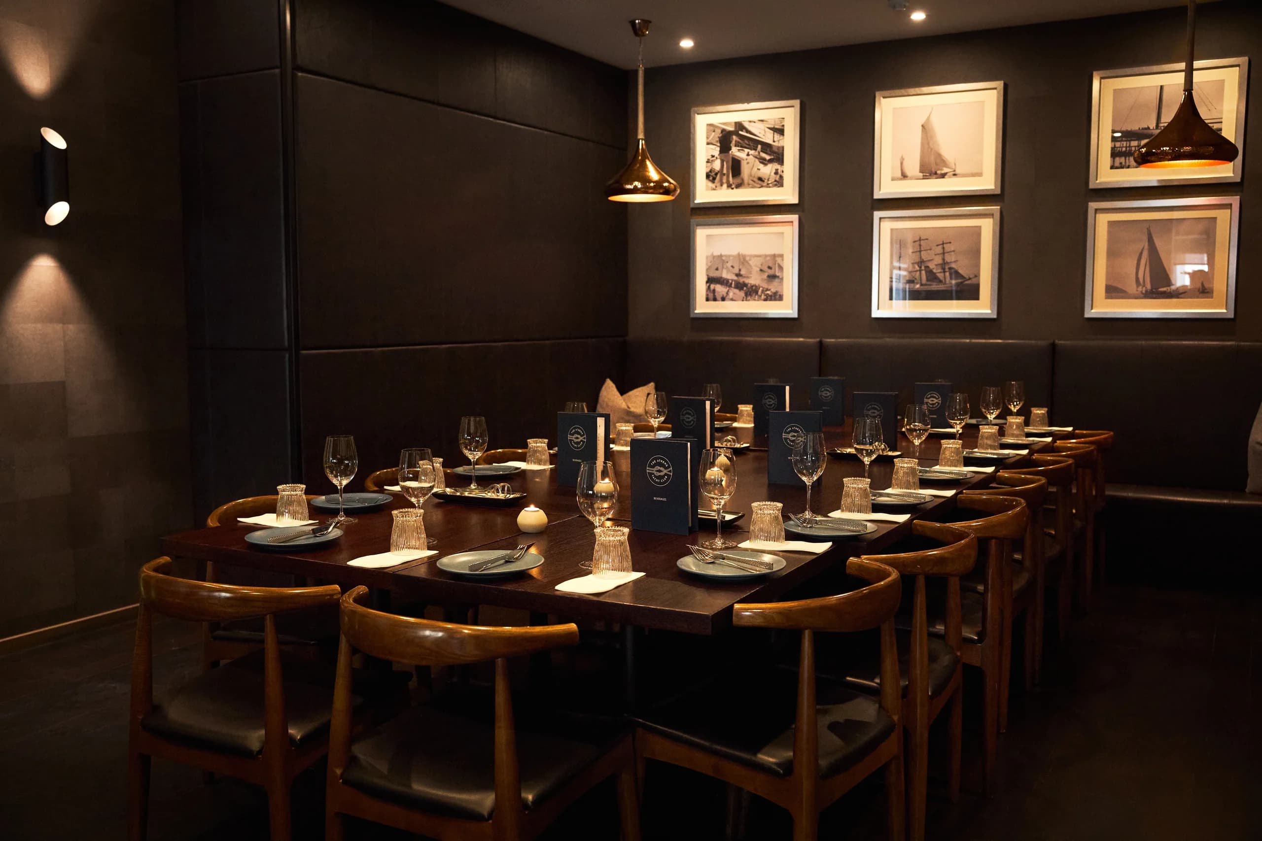Long table set for a private function beneath copper pendants and framed vintage sailing photographs