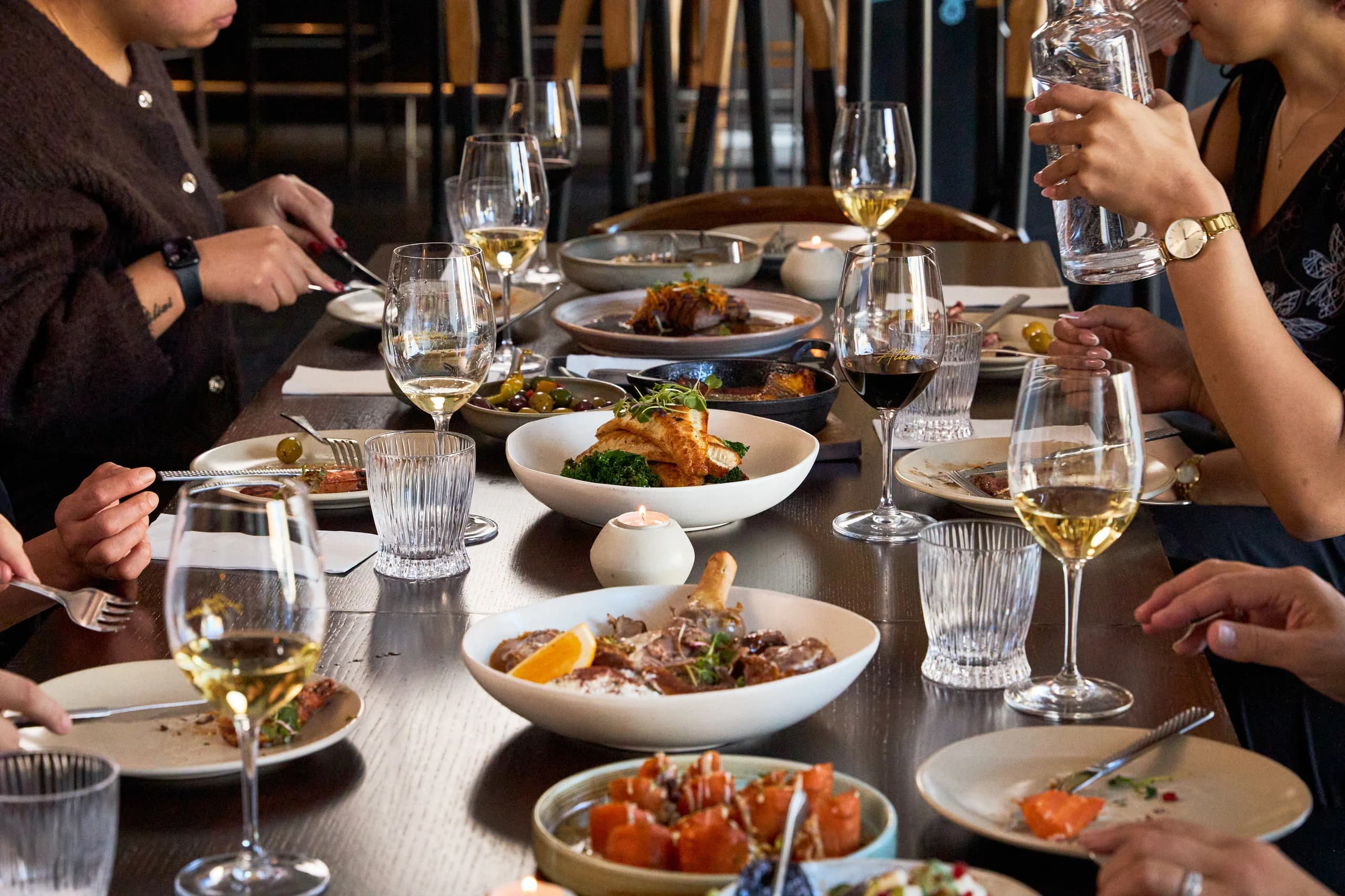 Long table with lamb on the bone, fish on greens, olives and carrots among candles and wine