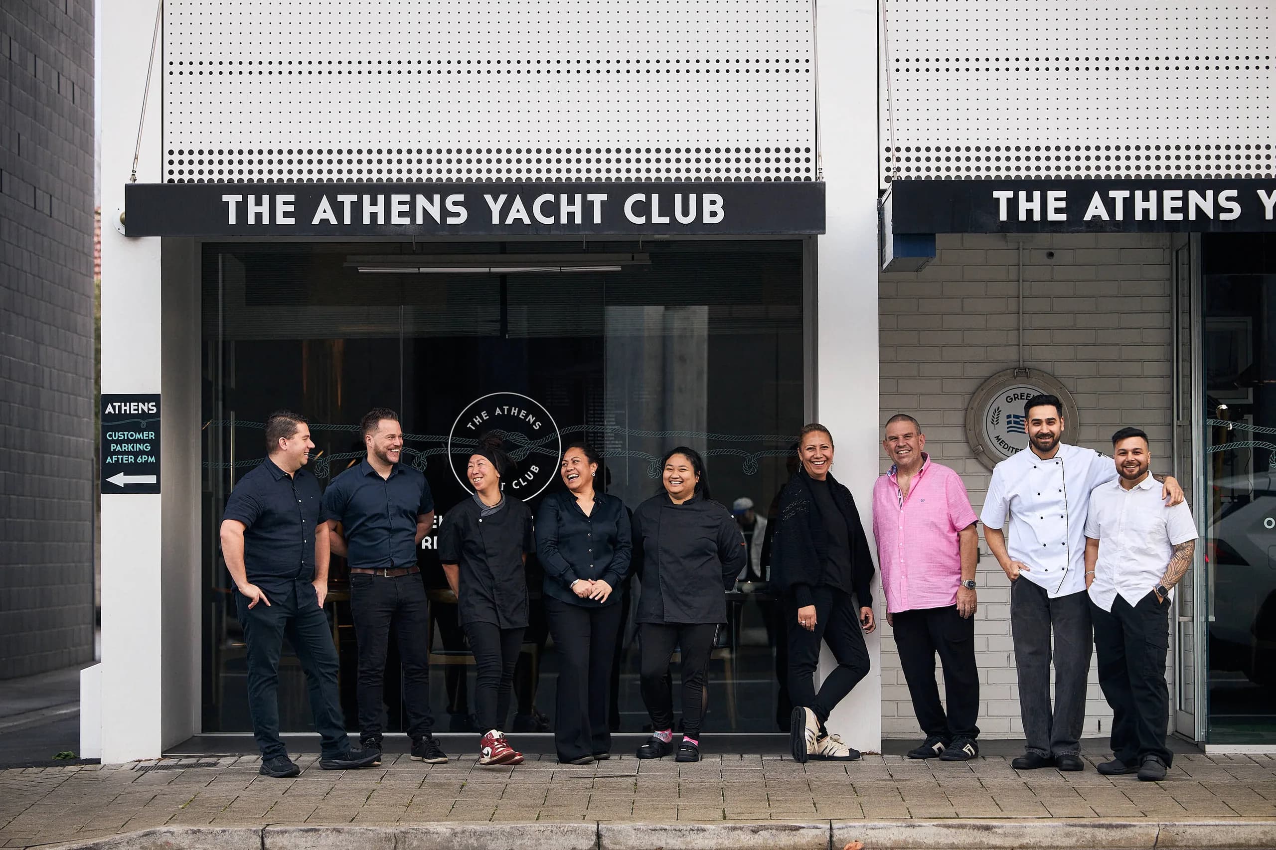 The Athens Yacht Club team, nine of them, laughing together on the footpath outside the restaurant